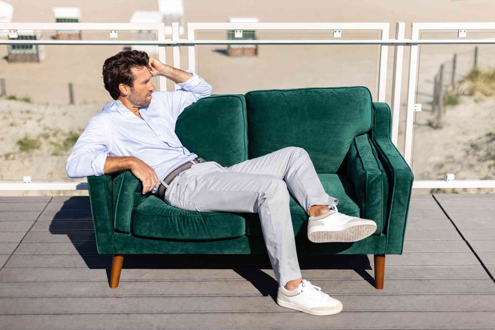 Grünes, samtenes 2-Sitzer Sofa von Club of Comfort mit dunklem Holzfarbton, Eichenholzbeinen, Armlehnen, Maßen 150x83 cm, Sitzhöhe 39 cm, gefüllt mit Schaumstoff, elastischer Gurtbandwellenfederung, auf Terrasse mit Blick aufs Meer.
