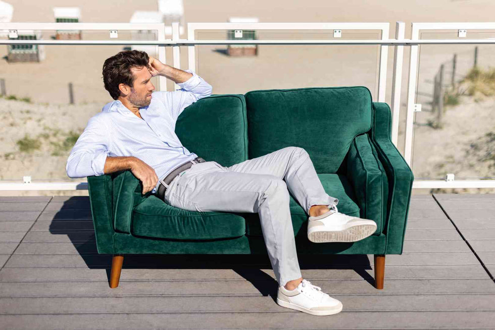Grünes, samtenes 2-Sitzer Sofa von Club of Comfort mit dunklem Holzfarbton, Eichenholzbeinen, Armlehnen, Maßen 150x83 cm, Sitzhöhe 39 cm, gefüllt mit Schaumstoff, elastischer Gurtbandwellenfederung, auf Terrasse mit Blick aufs Meer.