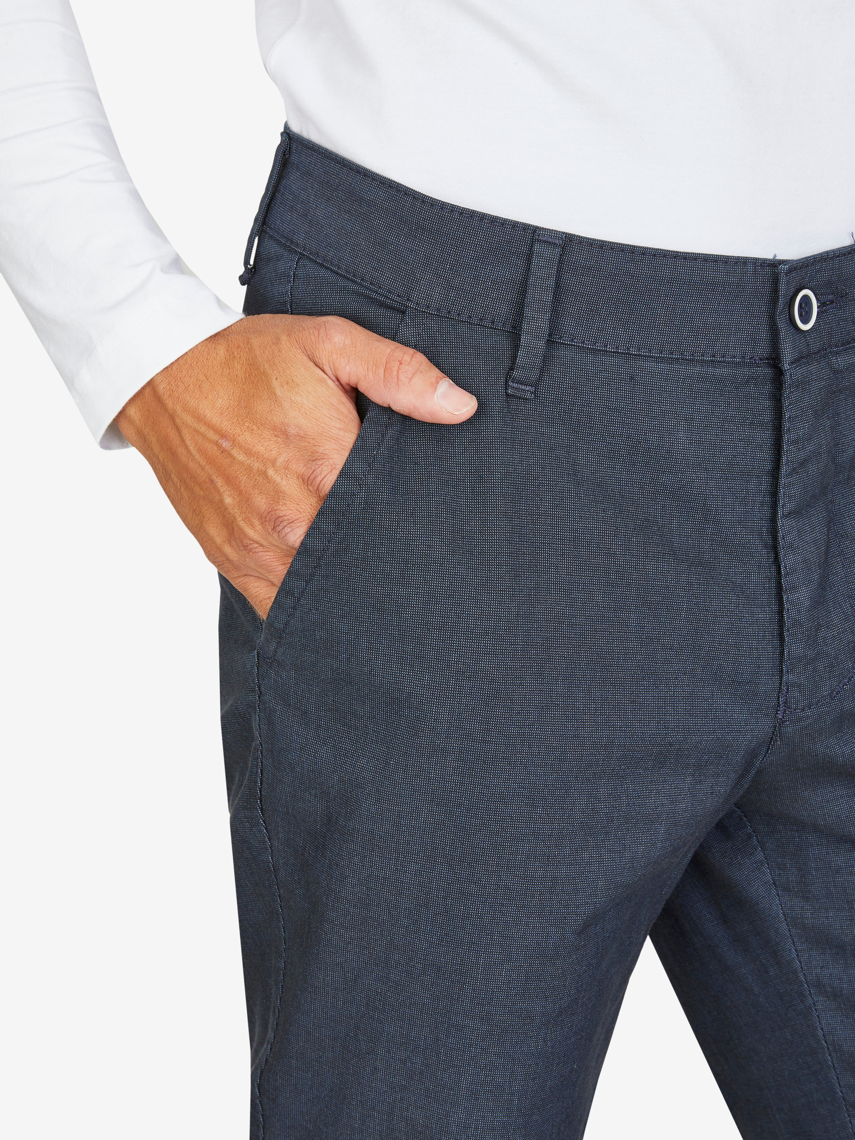 Nahaufnahme einer dunkelblauen, elastischen Flat Front-Hose mit Baumwoll-Mikrostruktur in Woll-Optik, mit Gürtelschlaufen und einer Hand im Bund. Modell zeigt Regular Fit, schmaler Beinverlauf, geeignet für Frühling/Sommer.