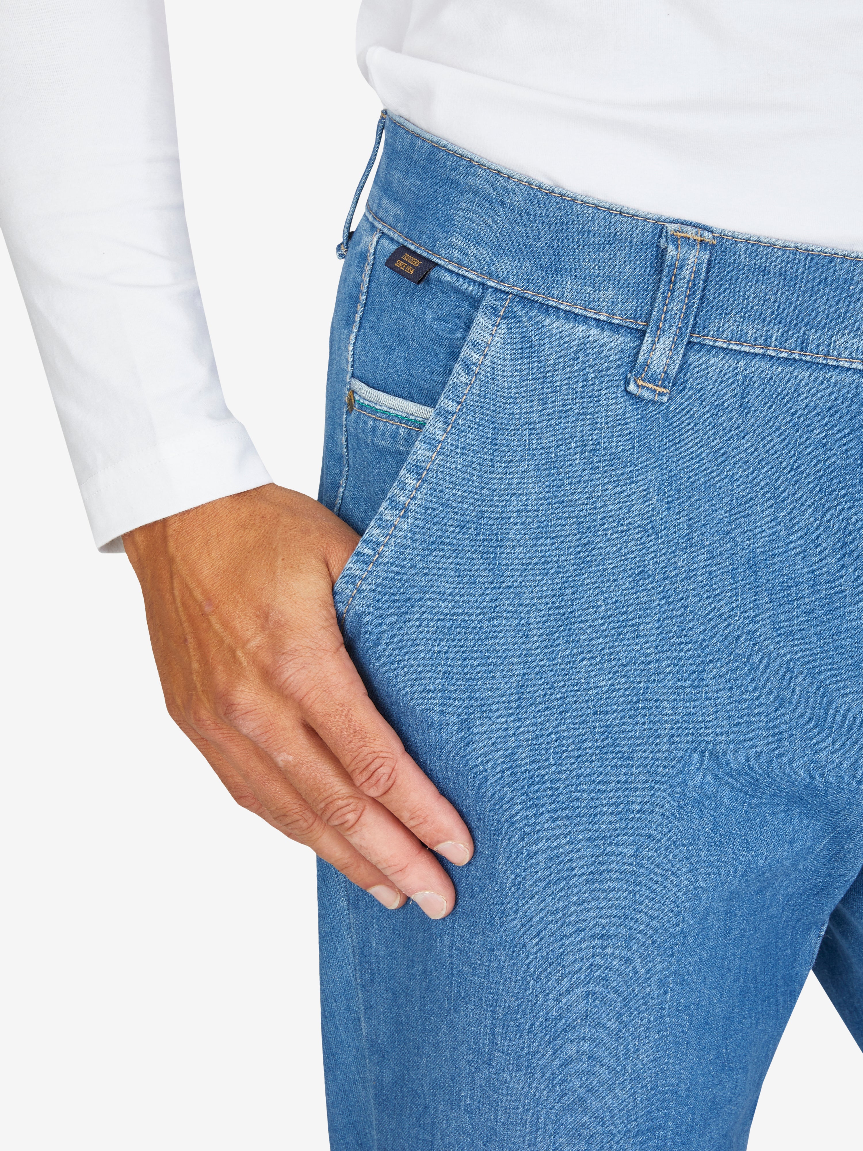Hose aus hellblauem Bi-Stretch-Denim mit Flat Front, elastischem Komfortbund und Hemdstopper, rechte Münztasche, schmaler Beinverlauf, normale Leibhöhe, getragen von einer Person in weißem Oberteil, Produkt von GARVEY/Club of Comfort.