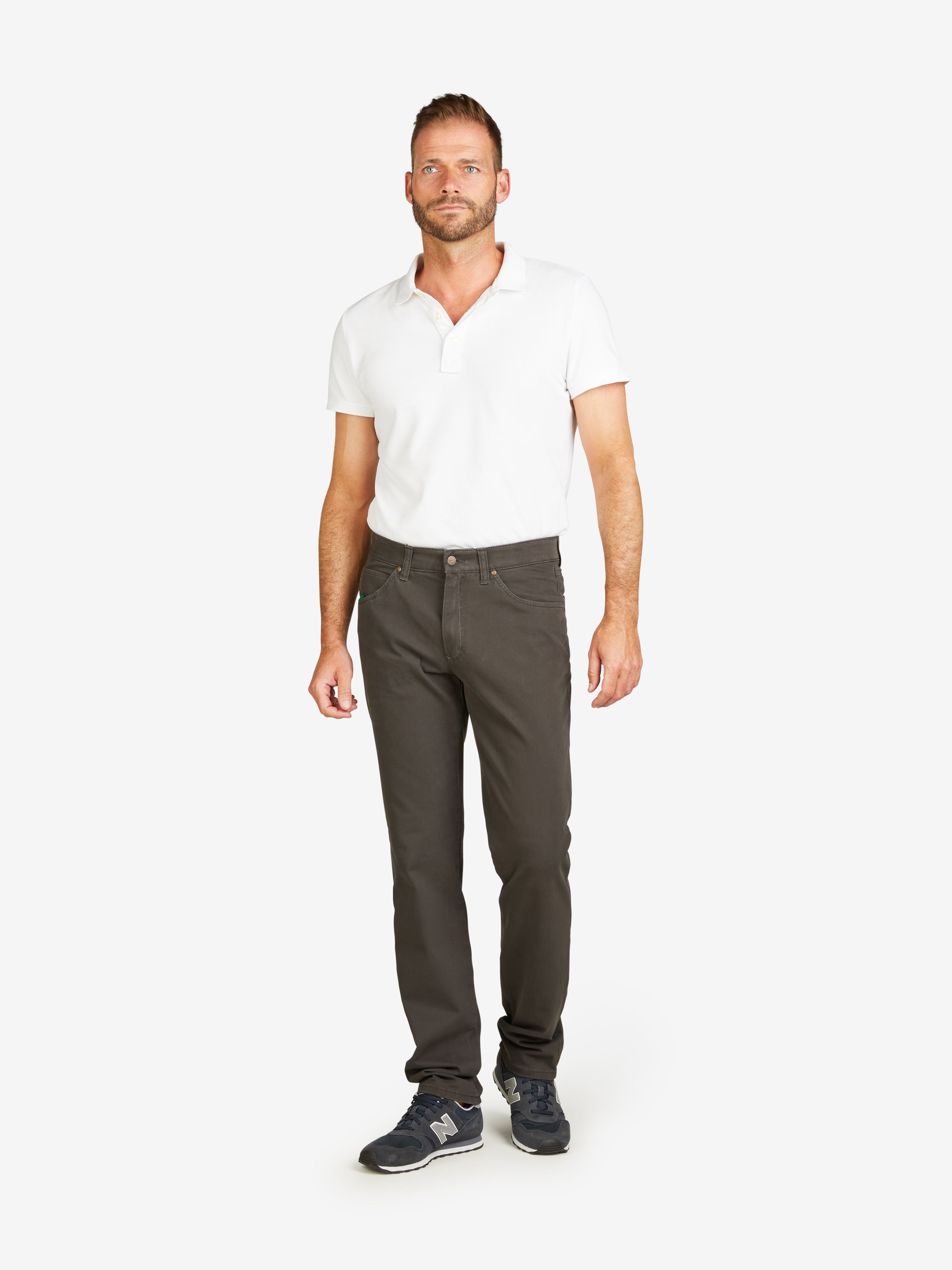 Mann trägt eine graue HENRY 8070 5-Pocket Baumwollhose mit Regular Fit, elastischem Doppelstoffbund, Hemdstopper und mobilem Smartphone-Täschchen in der rechten Vordertasche, kombiniert mit einem weißen Polo-Shirt und schwarzen Sportschuhen, vor neutralem Hintergrund.