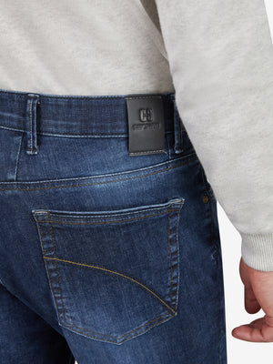 Nahaufnahme einer blauen, wasch 블au-beeigenen Flat Front-Hose von Club of Comfort mit elastischem Komfortbund, Hemdstopper und Bundverlängerung. Gefertigt aus hoch elastischem Super High Stretch-Denim mit 5-Pocket-Design, Tapered Fit und mittlerer Leibhöhe.