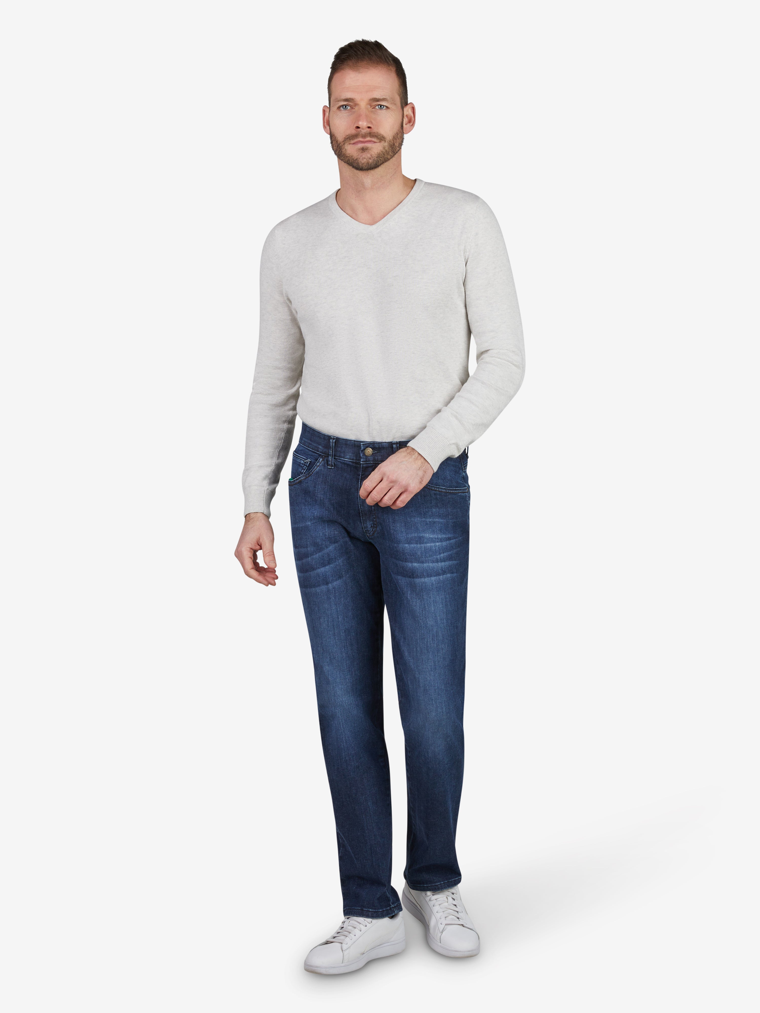 Mann trägt eine weiße, lange Ärmel Pullover und eine blaue, gewaschene ALEX 7915 Tapered Fit 5-Pocket Jeans mit elastischem Komfortbund, Hemdstopper und Bundverlängerung, aus super High Stretch-Denim mit Lycra dual-FX® Technologie, auf weißem Hintergrund.