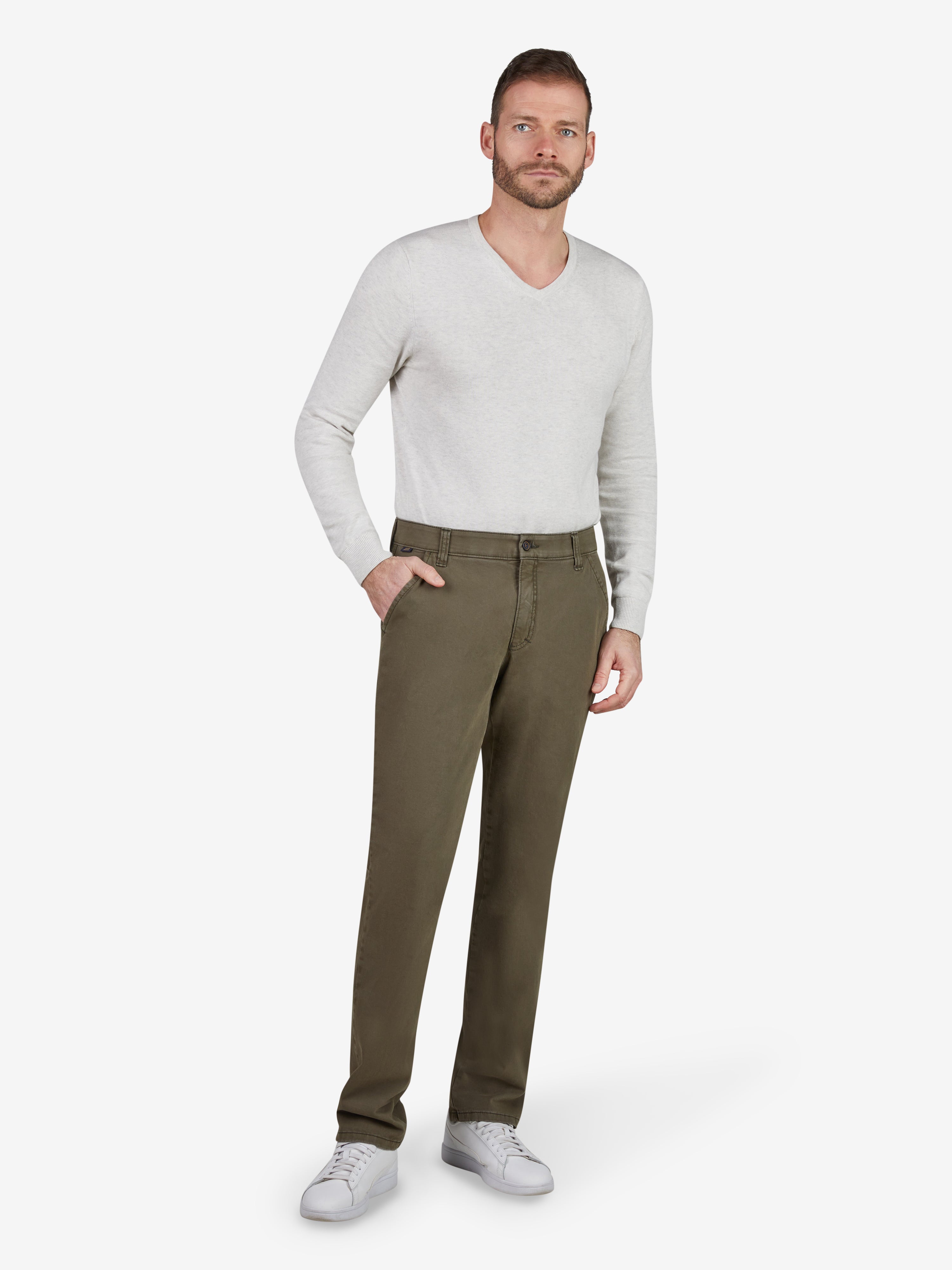 Mann trägt eine grüne GARVEY 8070 Flat Front-Hose aus bi-elastischer Baumwolle mit softem Griff, elastischem Komfortbund, Hemdstopper, Münztasche, normaler Leibhöhe, schlanker Beinform, kombiniert mit weißem Pullover und weißen Sneakers.