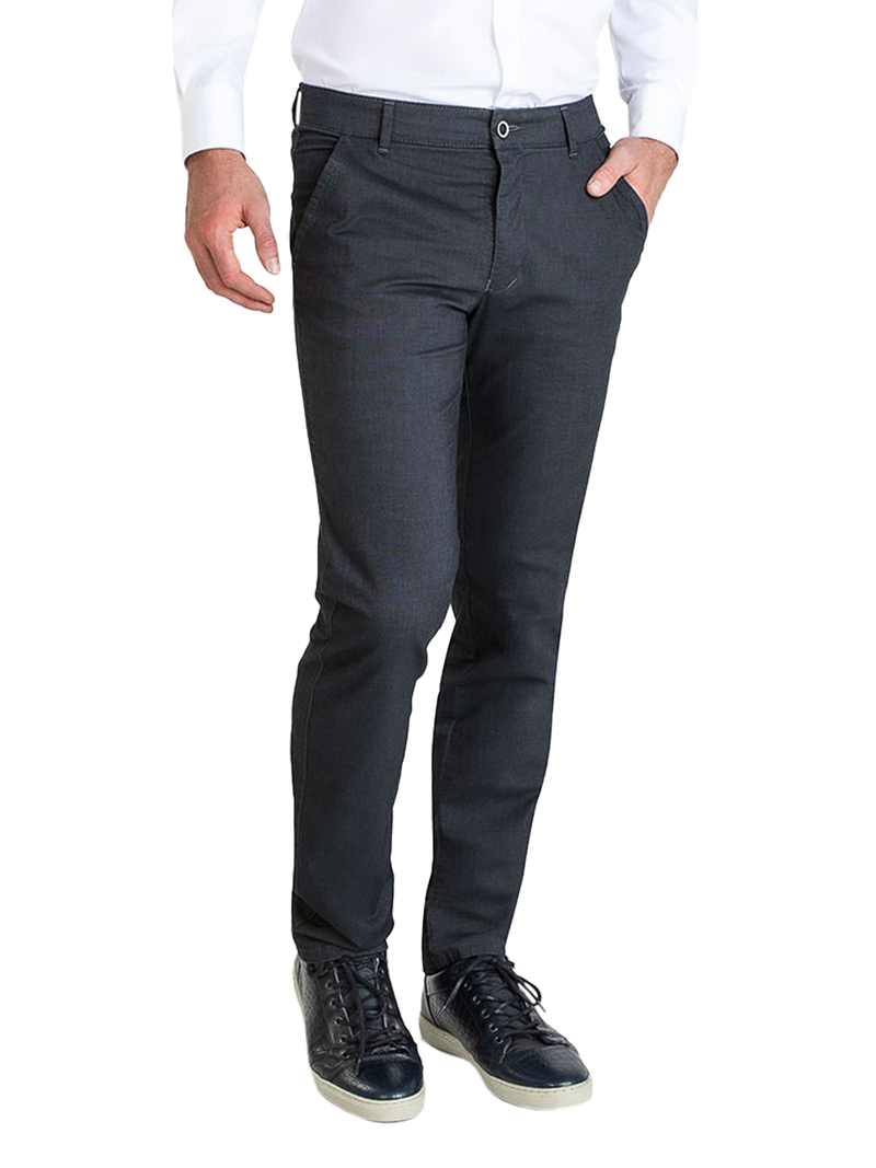 Ein Mann trägt eine weiße, langärmelige Hemd und dunkle, elegante Stoffhose mit Gürtel. Er hat eine Hand in der Hosentasche und trägt schwarze Sneakers.