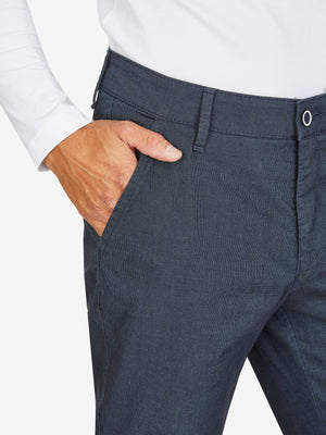 Nahaufnahme einer dunkelblauen, elastischen Flat Front-Hose mit Baumwoll-Mikrostruktur in Woll-Optik, mit Gürtelschlaufen und einer Hand im Bund. Modell zeigt Regular Fit, schmaler Beinverlauf, geeignet für Frühling/Sommer.