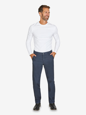 Mann trägt eine dunkelblaue GARVEY 6910 Flat Front-Hose mit elastischem Komfortbund, Hemdstopper und schmaler Fußweite, kombiniert mit weißem Langarmshirt. Die Hose ist aus Baumwoll-Mikrostruktur im Wool-Look, geeignet für Frühjahr/Sommer, mit Regular-Fit, Stretch und OEKO-TEX Standard 100.