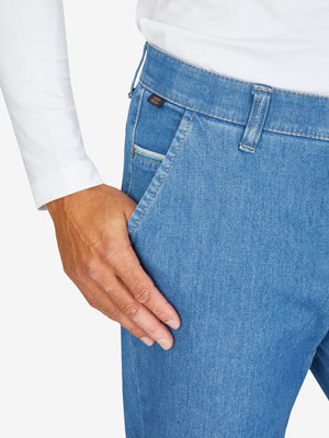 Hose aus hellblauem Bi-Stretch-Denim mit Flat Front, elastischem Komfortbund und Hemdstopper, rechte Münztasche, schmaler Beinverlauf, normale Leibhöhe, getragen von einer Person in weißem Oberteil, Produkt von GARVEY/Club of Comfort.
