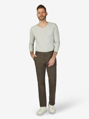 Mann trägt eine steingraue GARVEY 7612 Flat Front-Hose aus High Stretch-Baumwolle mit elastischem Komfortbund, Hemdenstopper, normaler Leibhöhe und schmaler Fußweite, kombiniert mit einem hellgrauen Pullover und weißen Sneakers, auf neutralem Hintergrund.
