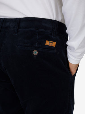 Nahaufnahme einer schwarzen Cord-Hose mit elastischem Komfortbund, Hemdenstopper und Knopf, getragen von einer Person in weißem Hemd, Produktmarkierung "GARVEY 8200" sichtbar.