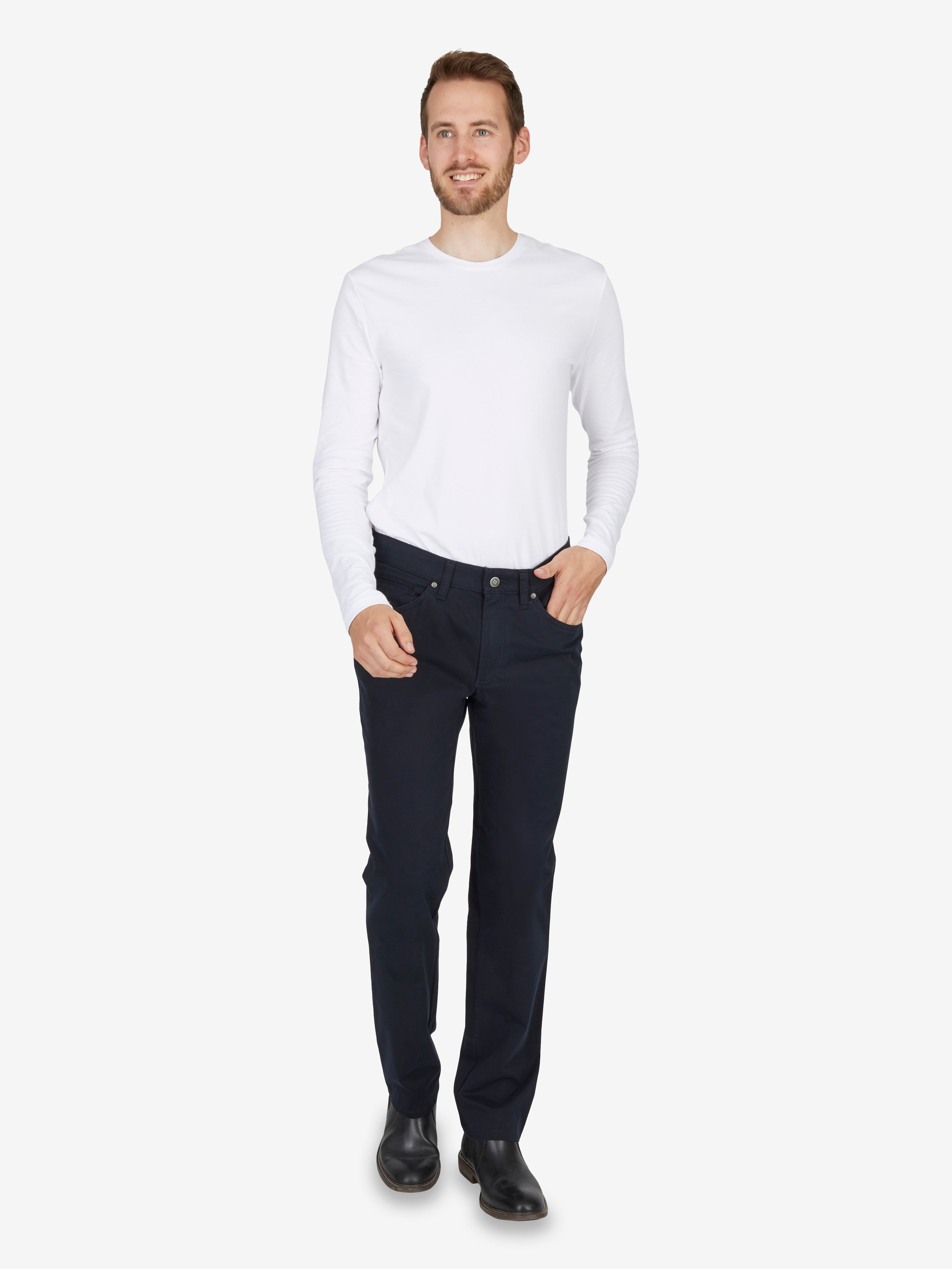 Mann trägt weiße Baumwoll-Hemd und dunkle 7-Pocket-Hose "HENRY-X7110" in Marine mit elastischem Doppelstoffbund, Mobile Pocket für Smartphone, Reißverschluss-Leistentasche, aus nachhaltigem High Stretch-Baumwollmaterial, Regular Fit, aufrechten, gepflegten Look.
