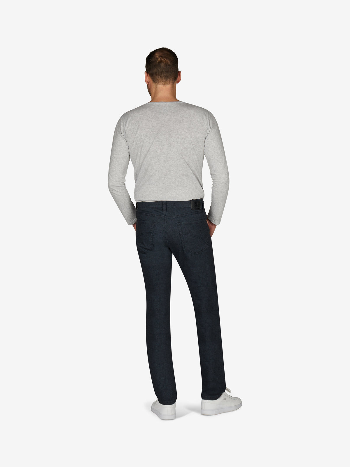 Ein Mann steht von hinten, trägt eine hellgraue, lange Ärmel-Shirt und eine dunkelblaue, schmal geschnittene 5-Pocket-Hose mit elastischem Bund, Mobile Pocket in der rechten Vordertasche, Münztasche mit Kontrast-Patch, aus Baumwoll-Woll-Struktur-Mischgewebe, für Herbst/Winter, in blau, Regular Fit, Schuhe weiß.