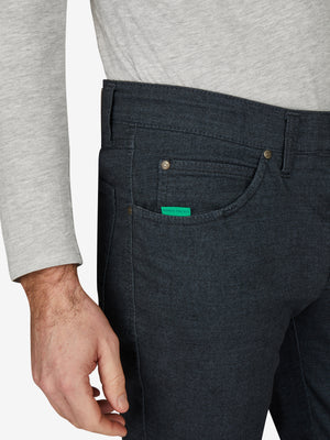 Nahaufnahme einer blauen Baumwollhose "HENRY 7631" in marine melange mit elastischem Doppelstoffbund, Hemdstopper, Münztasche mit Kontrast-Patch, und separater "Mobile Pocket" in der rechten Vordertasche. Dermodel trägt ein graues Oberteil.