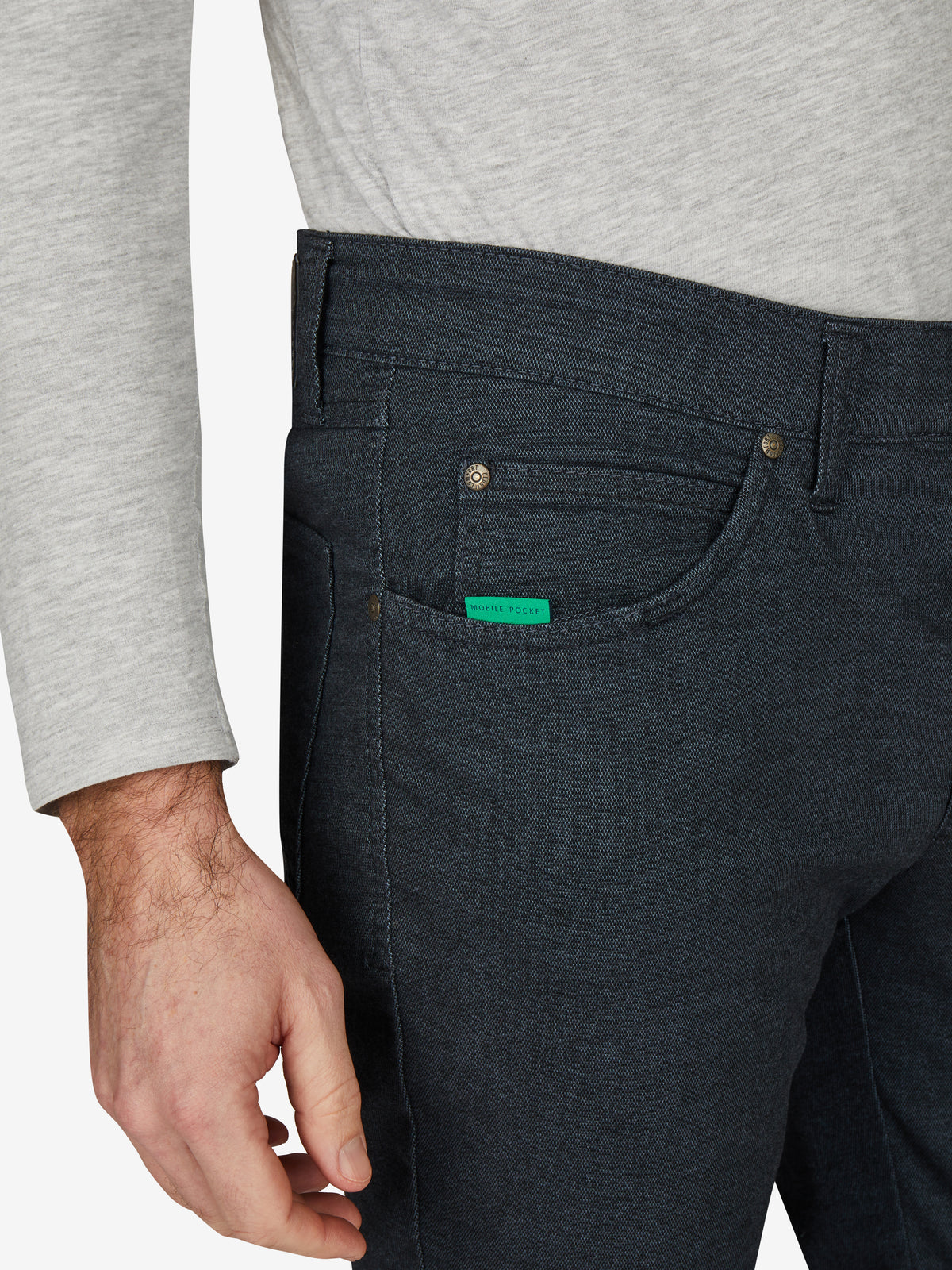 Nahaufnahme einer blauen Baumwollhose "HENRY 7631" in marine melange mit elastischem Doppelstoffbund, Hemdstopper, Münztasche mit Kontrast-Patch, und separater "Mobile Pocket" in der rechten Vordertasche. Dermodel trägt ein graues Oberteil.