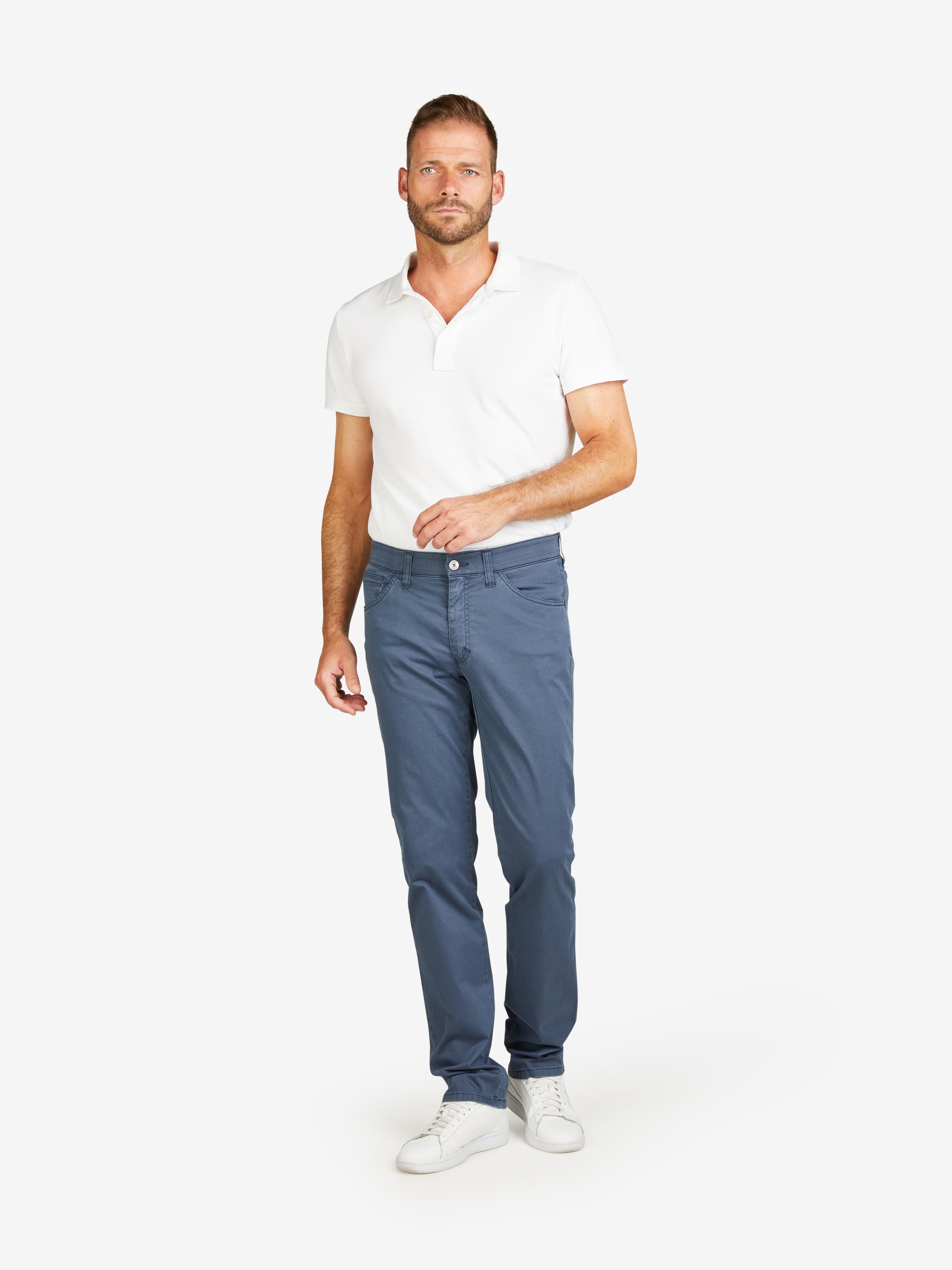 Mann trägt blaue MARVIN 8103 Hose von Club of Comfort mit regulärer Passform, elastischem Comfortbund, Hemdenstopper, Doppelpaspolierte Münztasche, leichtem Baumwoll-High-Stretch-Material mit Mikro-Print, gewichtet mit 270 g/lfm, Frühjahr/Sommer, Model in stehender Pose, weißes T-Shirt, weiße Sneakers.