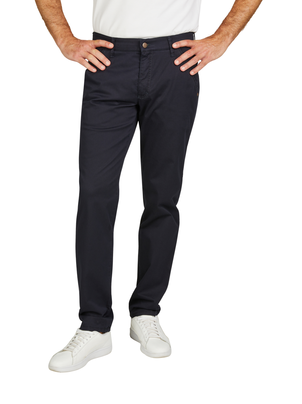 Hände eines Mannes, der eine weiße T-Shirt trägt, liegen auf der Hüfte. Er trägt dunkle, gerade geschnittene Hose und weiße Sneakers.