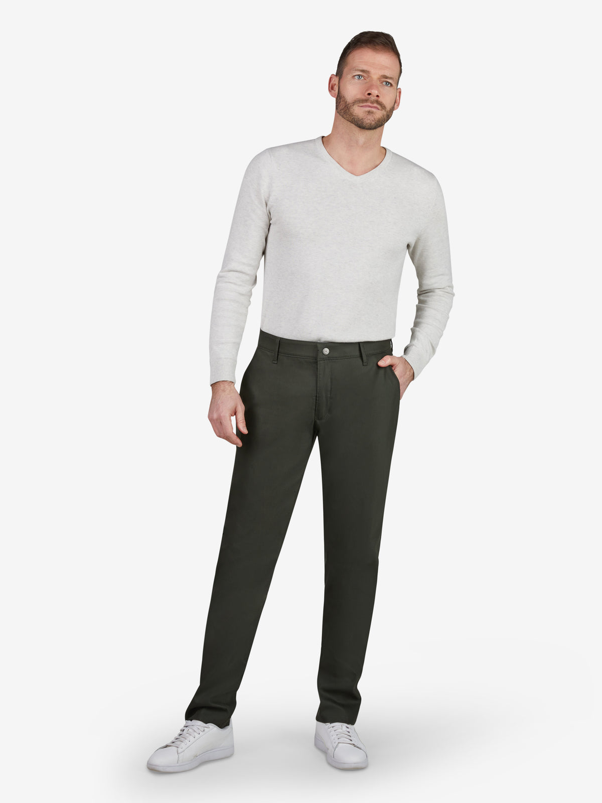 Mann trägt dunkelgrüne ROB 8130 Chino-Hose im Tapered Fit mit elastischem Comfortbund, Hemdenstopper und High Stretch aus Techno-Cotton, kombiniert mit weißem Pullover und Sneakers, vor hellgrauem Hintergrund.