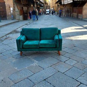 Grünes Club of Comfort Sofa, Samtstoff in Smaragdgrün, 2-Sitzer, mit Eichenholzfüßen, Maße: 150 x 83 cm, Höhe 85 cm, bequemes Polster mit Wellenfederung, geeignet für zwei Personen, in einer urbanen Straße.