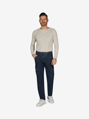 Männlicher Modell trägt eine blaue TANGO 8012 Cargohose im Tapered Fit mit elastischem Comfortbund, Hemdstopper, aufgesetzten Gesäßtaschen und Beintaschen mit Patte und Druckknopf, aus High Stretch Denim mit filigranem Warenbild, in einem hellen, neutralen Raum.