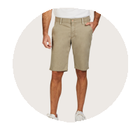 Ein Mann trägt beige Bermudashorts, ein graues T-Shirt und weiße Sneakers. Seine Hände sind in den Taschen der Shorts, der Blick ist nicht sichtbar.